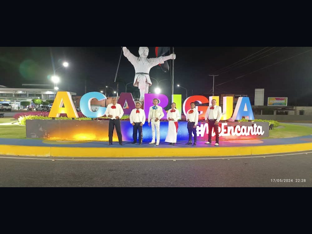 Mariachi Azteca de Acarigua de noche frente al letrero de Acarigua