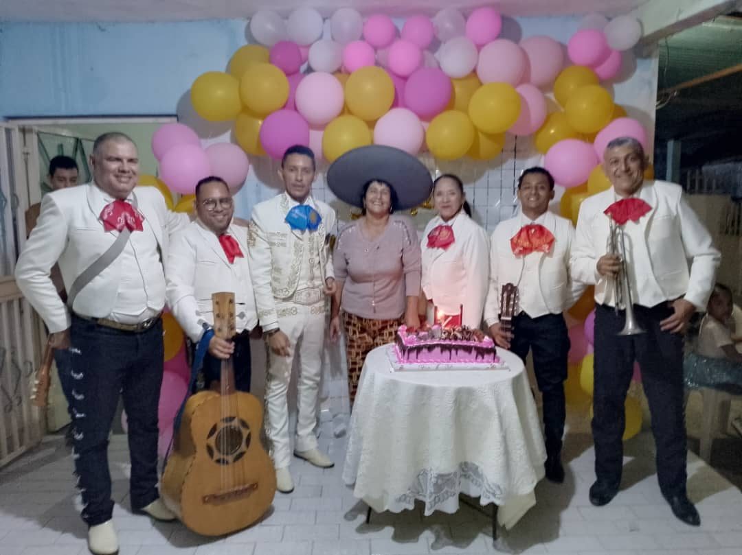 El mariachi con traje blanco en una serenata de cumpleaños con torta y globos